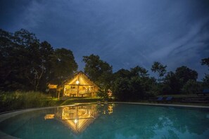 A house with a pool, surrounded by trees, at night.