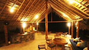 An outdoor lounge area with a stone bar, wooden furniture, and a thatched roof structure. - Gal Oya Lodge (MADULLA)