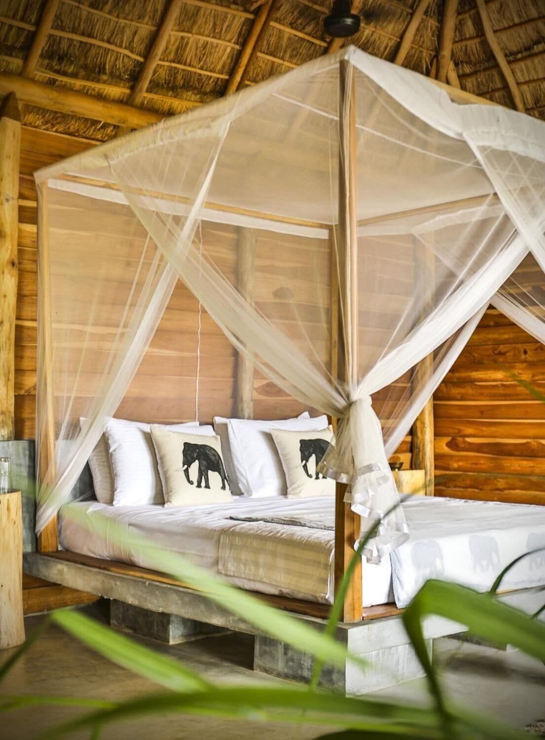 A bed with a canopy, wooden walls, and elephant-themed pillows.