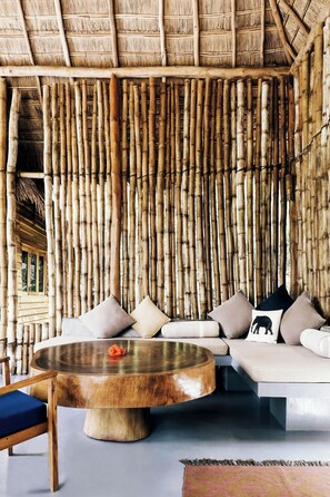A room with a bamboo wall, a round wooden coffee table, and a sofa with cushions. - Gal Oya Lodge (MADULLA)