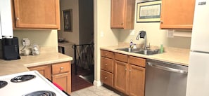 Una cocina con armarios de madera, un lavamanos de acero inoxidable, lavavajillas y estufa.