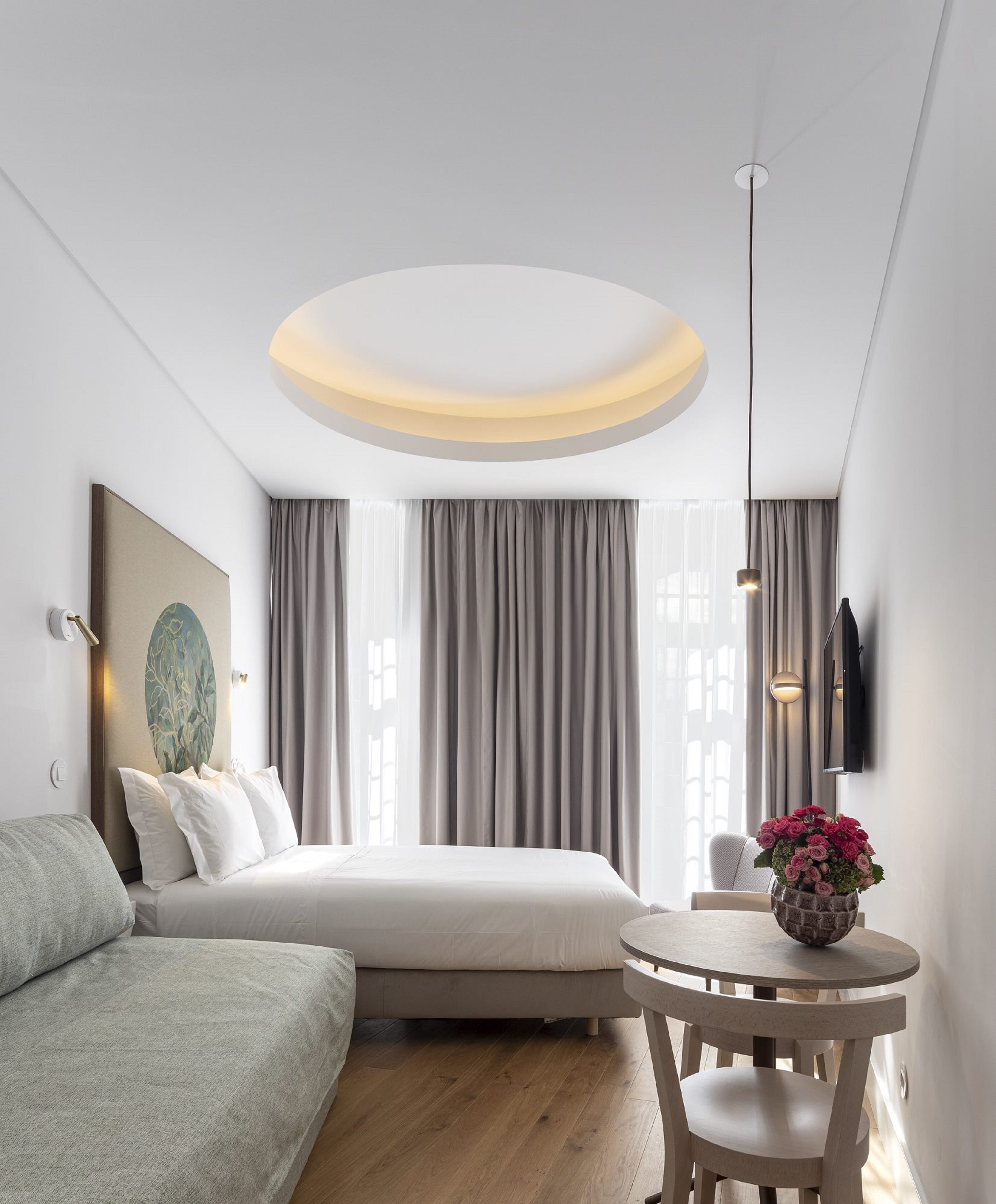 A modern hotel room with a bed, a round table, and a TV mounted on the wall.