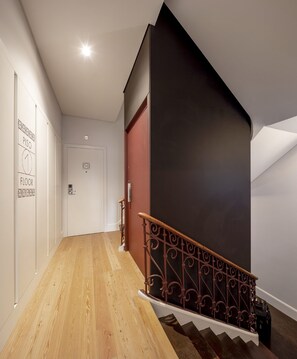 A hallway with a wooden floor, a staircase with a dark wall and metal railing, and a door labeled 'PISO 1 FLOOR'. - Lisbon Serviced Apartments Madalena (Lisbon)