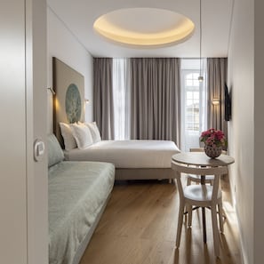 A modern hotel room with a bed, a sofa, a round table with a vase of flowers, and a large window with curtains. - Lisbon Serviced Apartments Madalena (Lisbon)