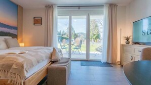 Ein Schlafzimmer mit Bett, Fernseher, Schreibtisch und einer Glastür zu einer Terrasse.