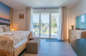 Ein Schlafzimmer mit Bett, Fernseher, Schreibtisch und einer Glastür zu einer Terrasse.