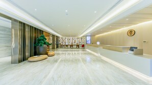 Un moderno vestíbulo de hotel con una recepción, zona de estar y una gran planta en maceta.