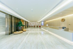 Un moderno vestíbulo de hotel con una recepción, zona de estar y una gran planta en maceta.