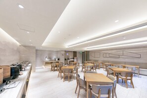 Un comedor moderno con mesas y sillas de madera, una zona de cocina con electrodomésticos y un diseño limpio y minimalista.