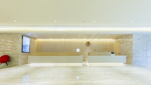 Un área de recepción moderna con suelo de mármol, mostrador de recepción, una silla roja y una pantalla fijada a la pared.