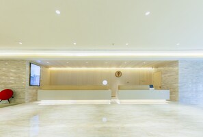 Un área de recepción moderna con suelo de mármol, mostrador de recepción, una silla roja y una pantalla fijada a la pared.