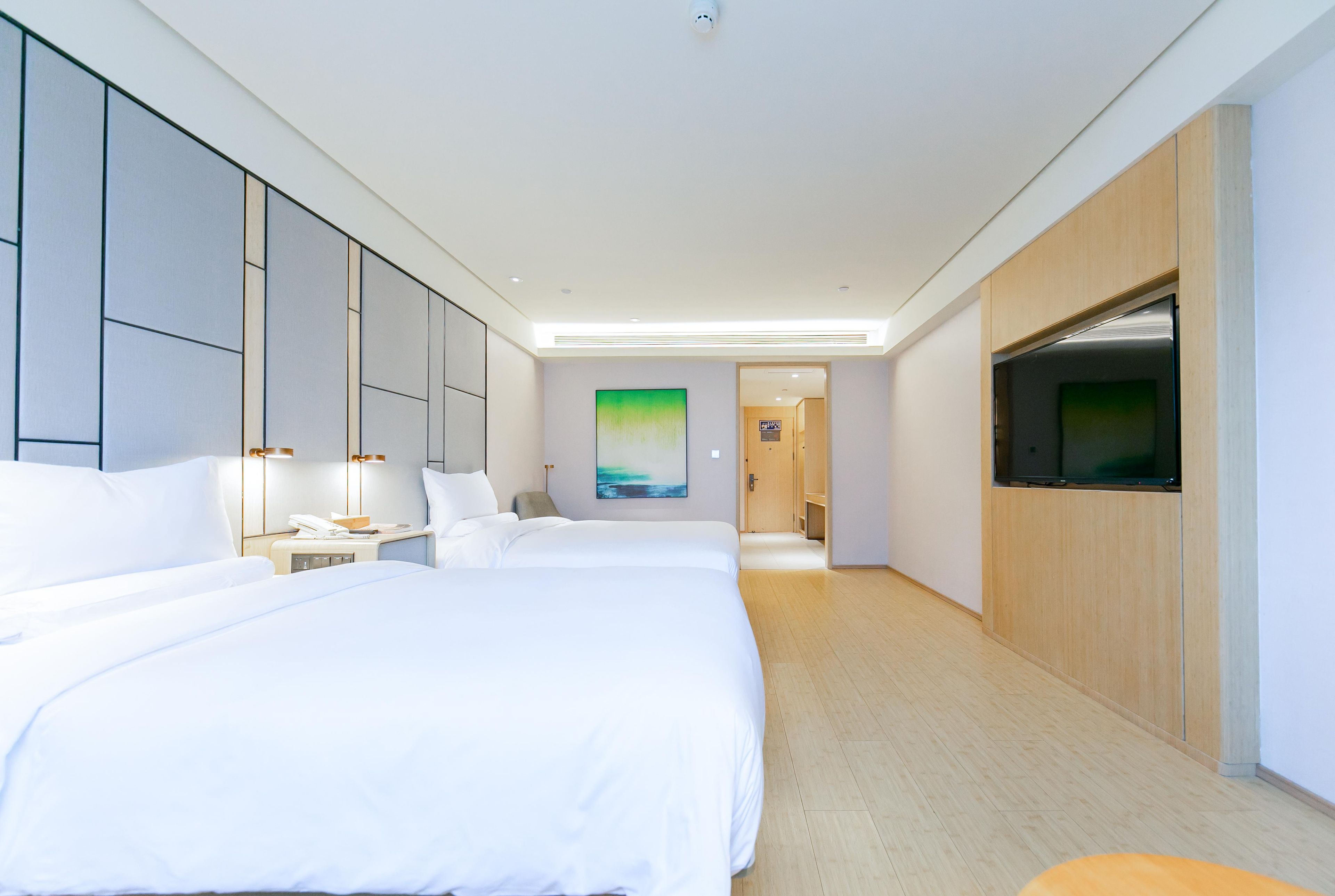 A hotel room with two beds, a TV, and a hallway leading to another room.