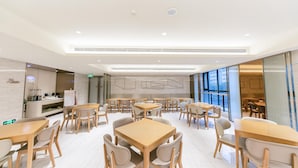 A modern dining area with wooden tables and chairs, a kitchen in the background, and large windows. - Ji Hotel (Luoyang)