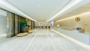 A modern hotel lobby with a reception desk, seating area, and a large potted plant. - Ji Hotel (Luoyang)
