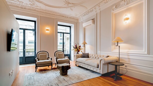 Un ampio soggiorno con soffitto alto, dettagli decorativi sul soffitto e una grande finestra, con una televisione a schermo piatto montata a parete.