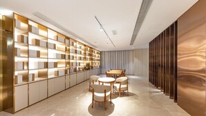 A modern interior with a long, narrow room featuring a central dining area with a wooden table and chairs, a built-in bookshelf with illuminated shelves, and a sleek, reflective wall on one side. - Ji Hotel Shanghai Jiayi Road Subway Statio (Shanghai)
