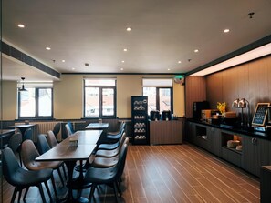 Un restaurant moderne doté d’une grande table conviviale, de sièges individuels, d’un comptoir avec une machine à café et offrant une vue sur la rue grâce à de grandes fenêtres.