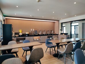 Une salle de conférence moderne, dotée d’une longue table, de plusieurs chaises, d’un coin cuisine et d’une grande fenêtre.