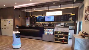 Ein modernes Café-Interieur mit einer Rezeption, digitalen Menütafeln und einem Selbstbedienungsgetränkeautomaten.