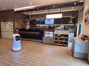 L’intérieur d’un café moderne, avec un comptoir d’accueil, des écrans numériques affichant le menu et un distributeur de boissons en libre-service.