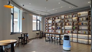 Ein modernes Interieur mit einer Holzbücherreolen, Tischen, Stühlen und einem Saugroboter.