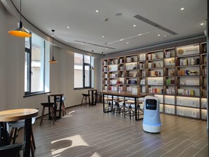 Un intérieur moderne avec une bibliothèque en bois, des tables, des chaises et un aspirateur robot.