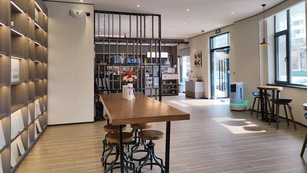 Ein modernes Interieur mit einem Holztisch, Barhocker und einer Raumtrennung mit Regalen.