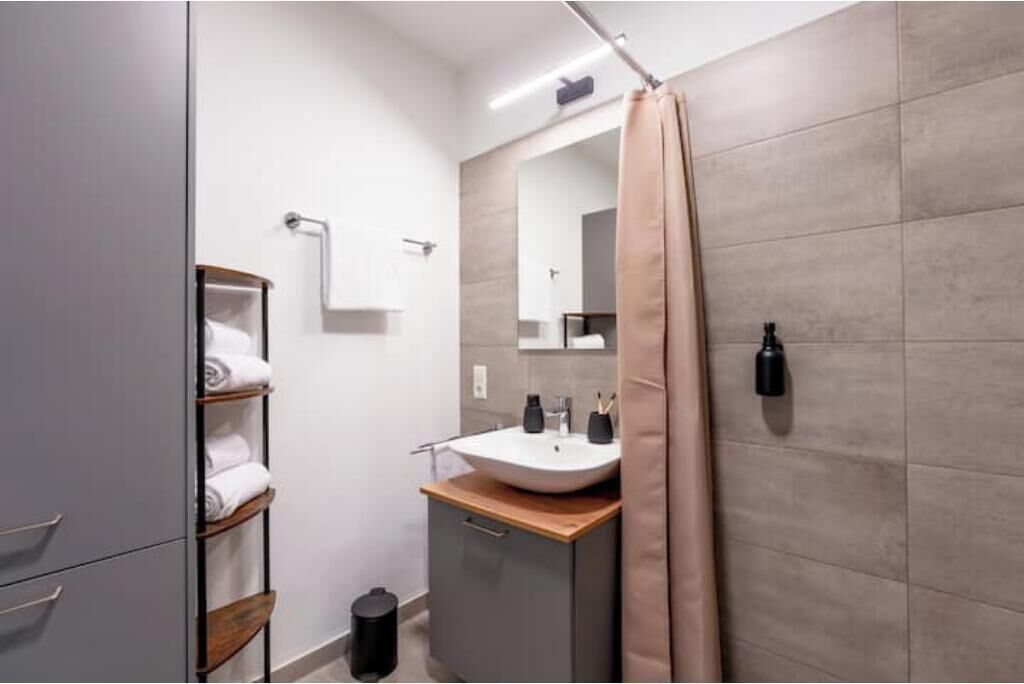 Une salle de bain moderne avec un grand miroir, un lavabo et un rideau de douche.