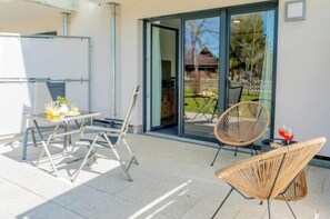 An outdoor seating area with a table and chairs, a whiteboard, and a sliding glass door leading to a garden. - 2-Bedroom Apartment with Living Room and Garden (Titisee-Neustadt)