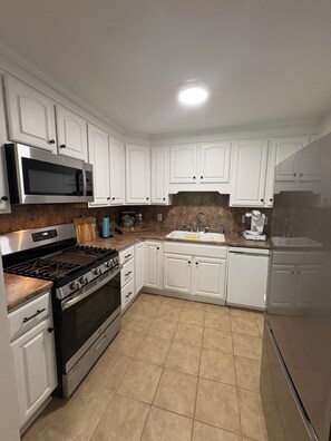 A kitchen with white cabinets, a stainless steel microwave, a stove, and a sink.