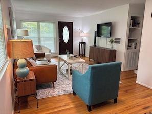 Una sala de estar con sofá, sillón, mesa de centro, lámpara, televisor y estantería.