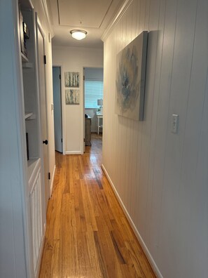 A hallway with wooden flooring, white walls, and a ceiling light.