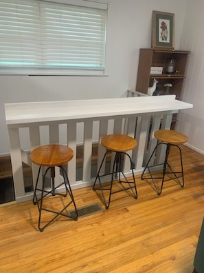 Un comptoir blanc avec trois tabourets en bois et une rambarde blanche.