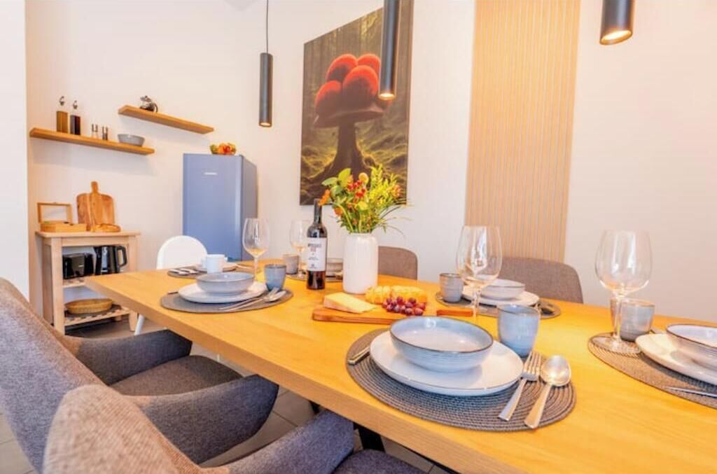 A dining area with a wooden table set for four, a blue refrigerator, and a painting of mushrooms on the wall.