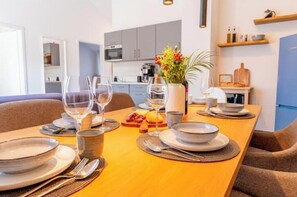 A dining table set with plates, glasses, and cutlery, with a kitchen in the background. - Stay | T9 3-room sky loft (Titisee-Neustadt)