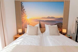 A double bed with two pillows, a nightstand with a lamp, and a wall-mounted painting of a mountain landscape. - Stay | T9 3-room sky loft (Titisee-Neustadt)