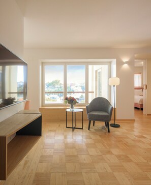 A modern living room with a wooden floor, a grey armchair, a small round table with a vase, and a large window offering a city view. - Lisbon Serviced Apartments - Principe Real (Lisbon)