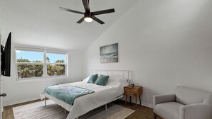 Un dormitorio con cama, ventilador de techo, ventana con vistas, mesita de noche y una silla.