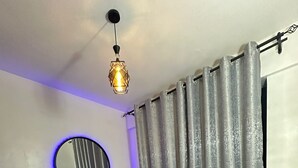 A bedroom with a bed, a mirror, curtains, and a hanging light fixture. - Perfect 1-bedroom apartment with fitness gym in the building (Nairobi)