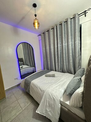 Un dormitorio con cama, espejo, cortinas y lámpara colgante.