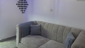A living room with a sofa, a coffee table, a wall-mounted light fixture, and a wall decoration. - Perfect 1-bedroom apartment with fitness gym in the building (Nairobi)