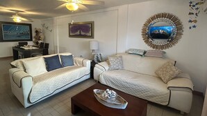 Un soggiorno con due divani, un tavolino, una ventola a soffitto, una TV a parete e un'area pranzo con tavolo e sedie.