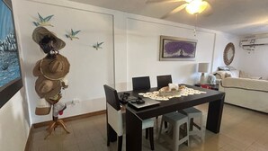 Zona pranzo con tavolo, sedie, ventilatore a soffitto e un quadro appeso al muro.