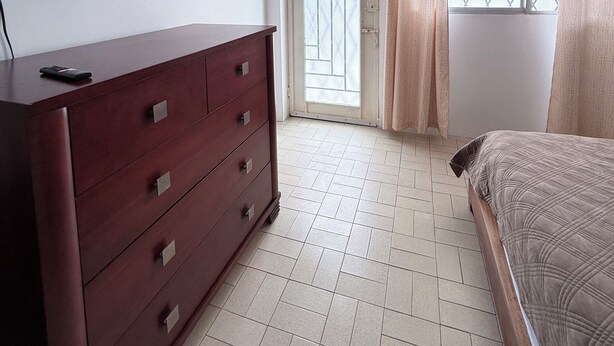 Una camera da letto con un letto, una cassettiera, una televisione a muro e una finestra con tende.