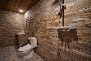 A bathroom with a stone wall, a toilet, a shower, and a sink. - Sunrise Penida Hill by ABM (Penida Island)