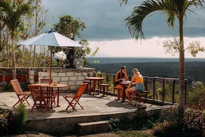 An outdoor patio with wooden furniture and a blue umbrella, overlooking a scenic landscape. - Sunrise Penida Hill by ABM (Penida Island)