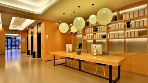 Een moderne hotel lobby met een lange receptiebalie, meerdere hangende sferische lampen en een boekenkast vol boeken.