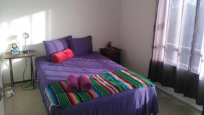 Une chambre à coucher avec un lit, une table de chevet, une lampe et une fenêtre avec des rideaux.