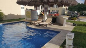 Une piscine avec des chaises longues, un parasol en chaume et un panneau indicateur.
