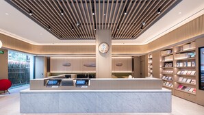 En moderne receptionsdisk med digitale skærme, en central søjle med et ur, og en reol fyldt med bøger til højre.